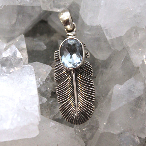 Silver feather-shaped pendant with a blue gemstone on a crystal background